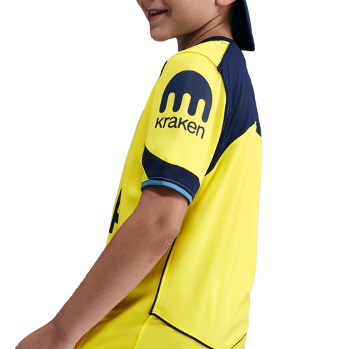 A profile view of a child wearing a yellow and navy blue sports jersey with a Kraken logo on the sleeve, against a black background.