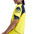 A profile view of a child wearing a yellow and navy blue sports jersey with a Kraken logo on the sleeve, against a black background.