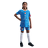 A young girl in a blue Atletico Madrid soccer kit with white socks and black cleats, posing with a hand on her hip against a black background.