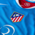 Close-up of a blue Nike athletic jersey featuring the Atlético Madrid crest and a red inner collar with a circular "90" logo.
