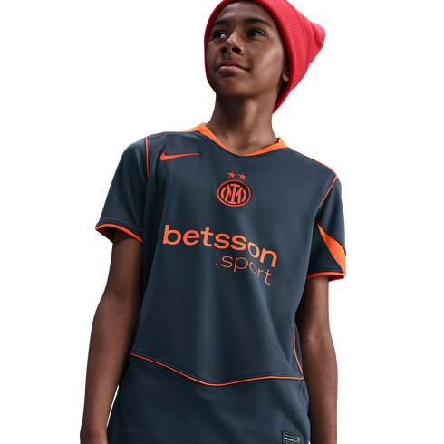 A young person wearing a red beanie and a grey Nike Inter Milan jersey with orange trim and "betsson .sport" branding, looking upward against a black background.
