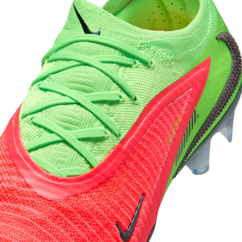 A close-up, high-angle view of a vibrant neon green and bright pink Nike soccer cleat against a black background. The shoe features a textured, knitted upper with matching neon green laces and multiple black Nike swoosh logos. Clear, translucent studs are