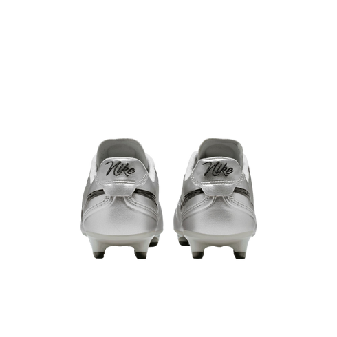 A rear view of a pair of metallic silver Nike soccer cleats with retro-style "Nike" script on the heels, set against a solid black background.
