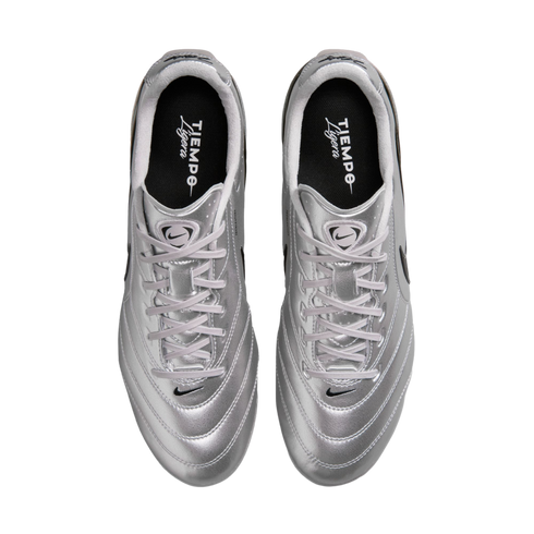 A top-down view of a pair of metallic silver Nike Tiempo Ligera soccer shoes with white laces and black insoles, set against a solid black background.