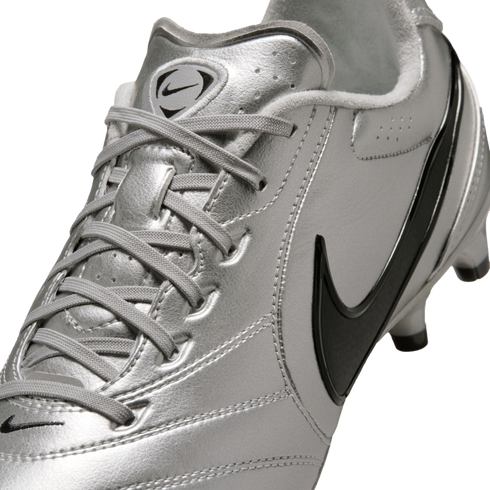 A close-up, angled shot of a metallic silver Nike soccer cleat featuring black swooshes and silver laces against a black background.