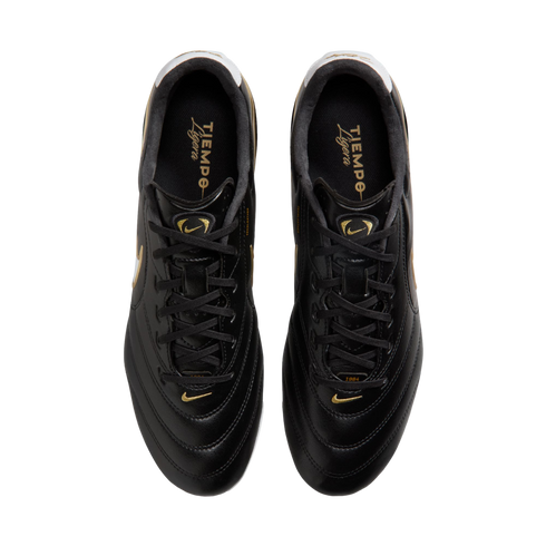 Top-down view of black Nike Tiempo Ligera soccer cleats with gold accents and branding, shown against a solid black background.