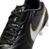 Close-up of a black leather Nike soccer cleat with black laces, gold branding on the tongue, and a white Nike swoosh with a gold border on the side.