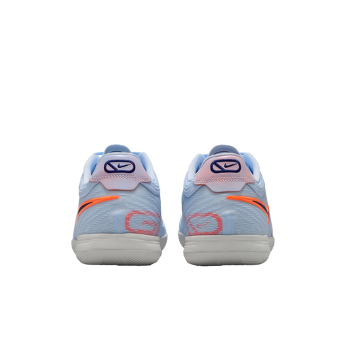 A rear view of a pair of light blue Nike performance sneakers featuring orange and coral accents, with a white textured sole, set against a solid black background.