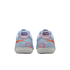 A rear view of a pair of light blue Nike performance sneakers featuring orange and coral accents, with a white textured sole, set against a solid black background.