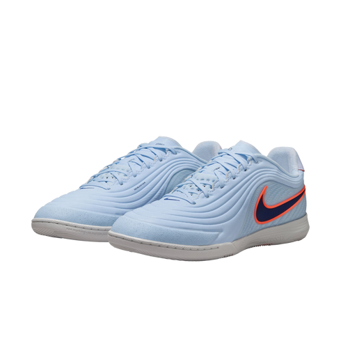 A pair of light blue Nike indoor soccer shoes with a dark blue swoosh outlined in bright orange. The shoes feature a textured, wavy upper design and a white rubber sole, shown against a solid black background.