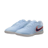 A pair of light blue Nike indoor soccer shoes with a dark blue swoosh outlined in bright orange. The shoes feature a textured, wavy upper design and a white rubber sole, shown against a solid black background.