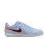 A side-view profile of a light blue Nike indoor soccer shoe against a black background. The shoe features a textured upper with wavy lines, a dark blue Swoosh with a bright orange outline, and a thin, white rubber sole.
