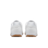 Rear view of a pair of white athletic shoes with tan gum soles, isolated against a black background.
