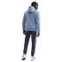 Rear view of a man with braids wearing a light blue hoodie and dark grey joggers against a black background.