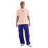 Full-length photo of a young man wearing a light orange Nike FC Barcelona t-shirt and purple cargo pants against a black background.