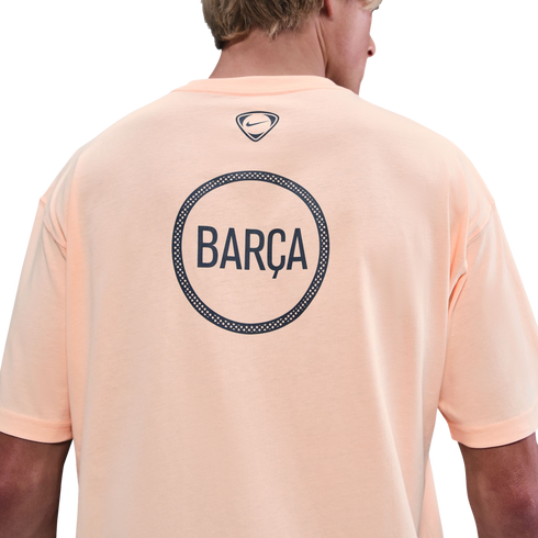 Back view of a person wearing a light orange Nike t-shirt with a large circular "BARÇA" graphic on the back against a black background.