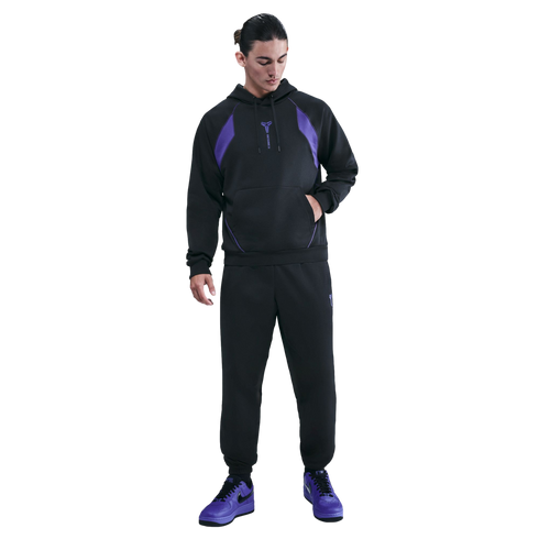 A man wears a black and purple Nike Kobe Bryant x FC Barcelona tracksuit and purple sneakers, standing against a black background.