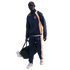 A man wearing a navy and orange Nike FC Barcelona tracksuit carries a black duffel bag against a solid black background.