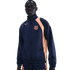 A man wearing a navy blue and peach Nike FC Barcelona windbreaker tracksuit against a black background.