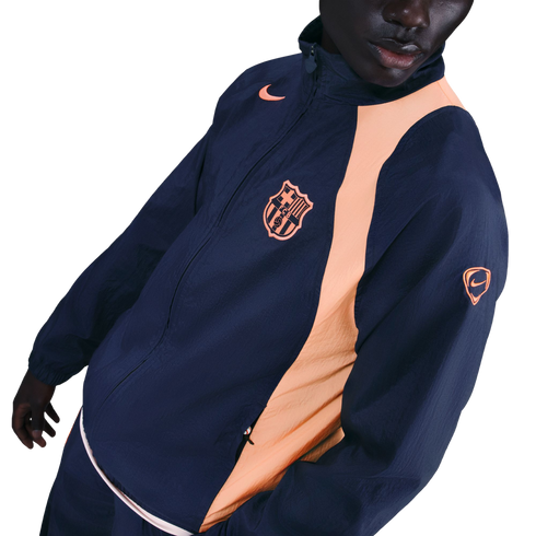 A person wearing a navy blue Nike FC Barcelona windbreaker with peach accents and the team's crest on the chest.