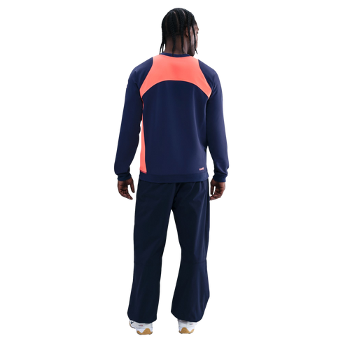 Rear view of a person wearing a navy tracksuit with a bright orange panel across the upper back, against a black background.