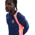 Man with braids wearing a navy and pink Nike FC Barcelona long-sleeve training shirt, looking away against a black background.