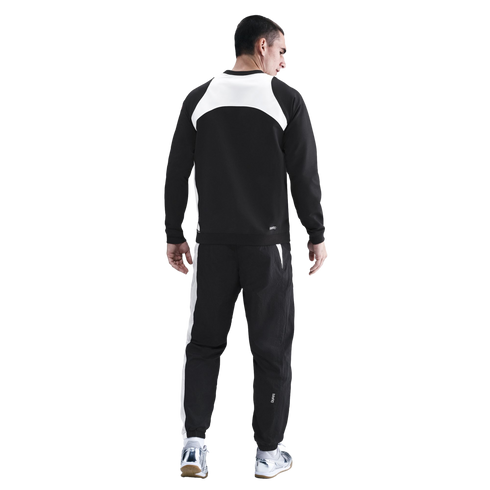 Rear view of a man wearing a black and white tracksuit and silver sneakers against a black background.