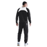 Rear view of a man wearing a black and white tracksuit and silver sneakers against a black background.