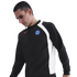 A man looking down while wearing a black and white Paris Saint-Germain long-sleeve sweatshirt with a red Nike logo against a black background.