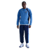 Man wearing a blue Tottenham Hotspur Nike sweatshirt, navy track pants, and blue and white sneakers against a black background.