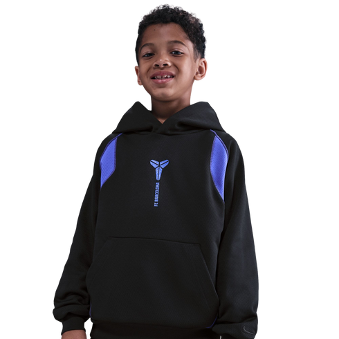 A smiling young boy with curly hair wearing a black Nike hoodie with a blue Kobe Bryant logo and "FC Barcelona" text, isolated against a solid black background.