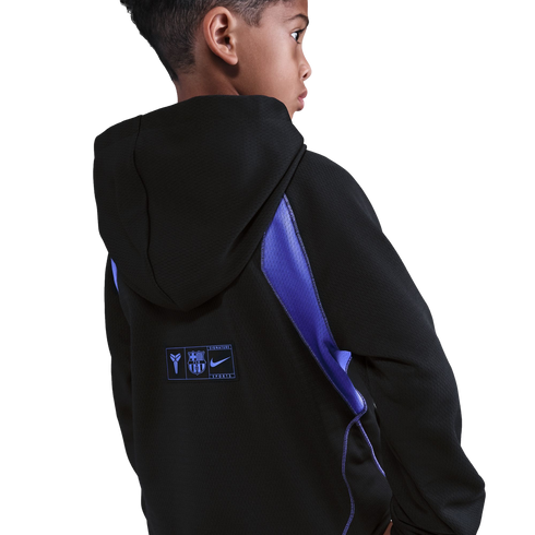 Back view of a boy in a black hoodie with blue mesh accents. A patch on the lower back features the Kobe Bryant, FC Barcelona, and Nike logos.
