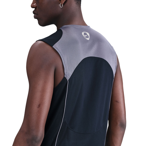 Back-angle view of a person wearing a grey and black Nike sleeveless mesh athletic top, set against a solid black background.