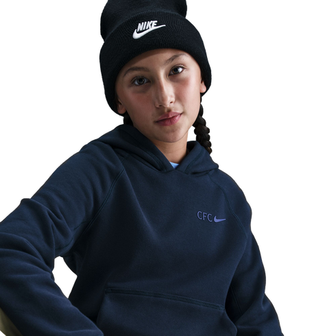 A young person wearing a black Nike beanie and a navy blue hoodie with a "CFC" Nike logo, posed against a solid black background.