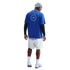 Rear view of a man wearing a blue CFC t-shirt over black long sleeves, white shorts, a grey beanie, and Nike sneakers against a black background.
