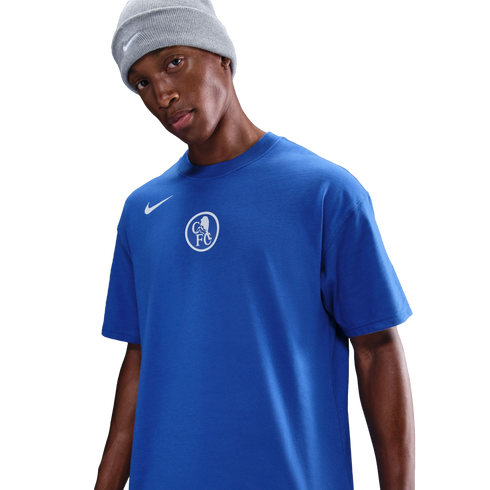 A man in a grey Nike beanie and a blue Nike Chelsea FC t-shirt with a white central crest, set against a black background.