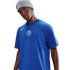A man in a grey Nike beanie and a blue Nike Chelsea FC t-shirt with a white central crest, set against a black background.