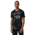 A man with a buzz cut models a black Paris Saint-Germain jersey and shorts featuring an iridescent marbled pattern, the Qatar Airways sponsor logo, and Jordan Brand's Jumpman logo, set against a solid black background.