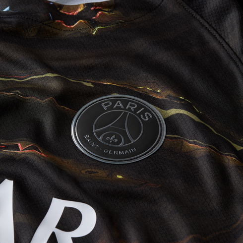 Close-up of a dark, marbled-pattern jersey featuring the Paris Saint-Germain club crest in a matte black and silver finish.
