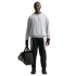 Full-length shot of a man in a grey pullover and navy track pants, holding a black duffel bag with blue cleats against a black background.