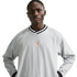 A man in a light grey Nike windbreaker shirt with a striped v-neck and orange lion crest, posing against a black background.