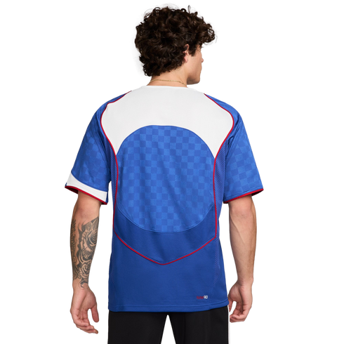 Back view of a man with curly hair wearing a blue soccer jersey with a white yoke, red trim, and a checkered pattern on the back.