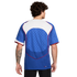 Back view of a man with curly hair wearing a blue soccer jersey with a white yoke, red trim, and a checkered pattern on the back.