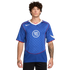A man with curly hair wearing a blue Nike Total 90 soccer jersey with a white "90" logo and checkered pattern.