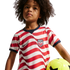 A young child with curly hair wearing a red and white striped USA soccer jersey holding a yellow soccer ball against a black background.