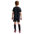 Rear view of a young boy with red hair wearing a black soccer kit with a star pattern and red trim. He is standing against a solid black background, wearing tall black socks with "U.S.A." in red and pink soccer cleats.