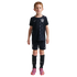 A young boy with red hair standing against a black background, wearing a dark blue Nike USA soccer kit with matching shorts, black socks, and pink cleats.