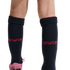 A close-up of a person's lower legs against a black background, wearing navy blue knee-high socks with a red script logo and a glimpse of a pink and orange athletic shoe.