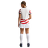 Rear view of a person in a white sports jersey with red wavy stripes, a white pleated skirt, and knee-high socks against a black background.