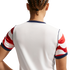 Back view of a person with braided hair wearing a white sports jersey with red and white patterned sleeves and navy blue trim.